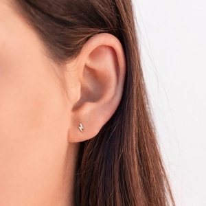 Detailed view of a small golden lightning bolt stud earring worn by a female model