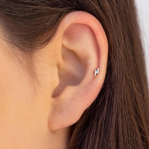 Macro view of gold lightning bolt stud earrings on ear for minimalist jewelry style
