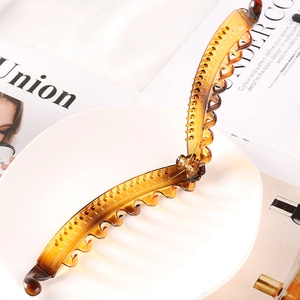 Detail of amber plastic banana hair clip with teeth on a white plate and magazine