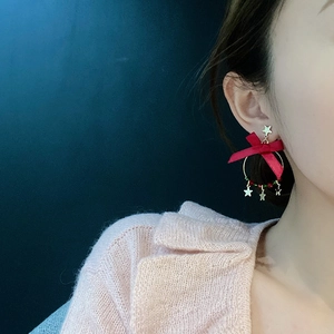 Close-up of red ribbon bow earrings with golden star charms on a female model