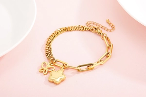 Dettaglio del bracciale dorato con farfalla e maglie rettangolari su sfondo rosa delicato