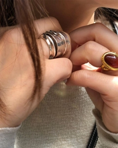 Detail of silver textured wide leaf ring and gold ring with red gemstone on fingers