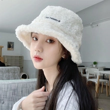 Close-up of white plush bucket hat with YI Talento M embroidery in a cafe setting