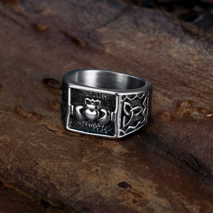 Vintage stainless steel Claddagh ring with Celtic knots on a textured wood surface