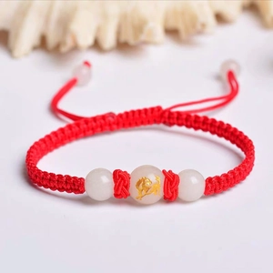 Close-up of handmade red woven bracelet with a luminous bead and golden zodiac patterns