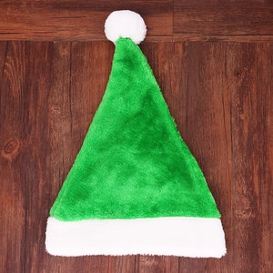 Flat lay of green plush Christmas hat with white pom-pom on wooden floor background