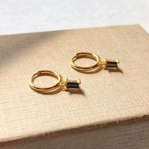 Detail of gold hoop earrings with emerald-cut black gemstone drops on wooden stand