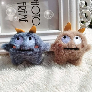 Macro shot of cute plush monster brooches in grey-blue and light brown with soft fur