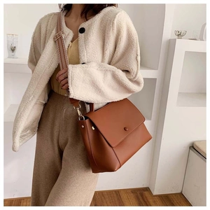 Detail of brown leather crossbody bag featuring a geometric patterned wide woven shoulder strap