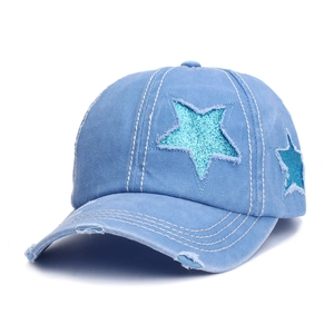 Close-up of distressed light blue denim baseball cap with sequin star patches and frayed holes