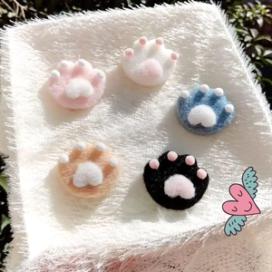 Cartoon plush cat paw brooches in five colors on soft white fabric background