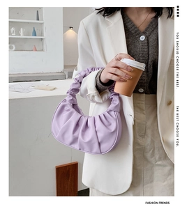 Detail of light purple pleated cloud bag held by a model in a minimalist urban setting