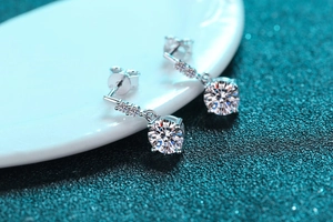 Macro shot of silver four-prong earrings with round cut moissanite on a white ceramic tray