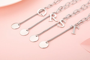 Detailed view of silver initial pendants Q, R, S, T on a soft pink background