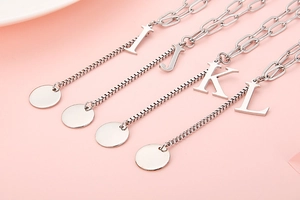 Detail of silver letter pendants I, J, K, L with round charms on a pink background