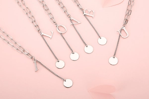 Detailed view of silver letter necklaces spelling I Love U on romantic pink background