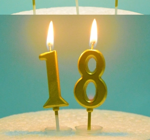 Close-up of golden number 18 candles burning on a white frosted cake topper