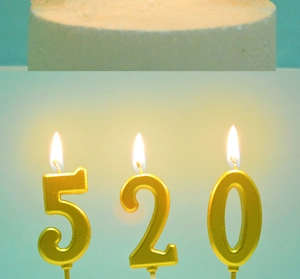 Close-up of lit gold number candles 5, 2, 0 on cake with warm ambient lighting