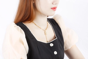 Detail shot of a gold letter R necklace with a sleek metal tassel on a white background