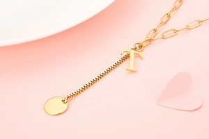 Detail of golden paperclip chain necklace with 3D letter T pendant and round tag