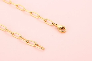 Close-up of gold paperclip chain necklace with a secure lobster clasp on pink background