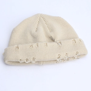 Detail of distressed knit beanie with metal rings and safety pins in cream white color