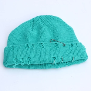 Detail of teal knit beanie featuring silver safety pin and triple ring metallic accents