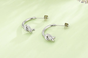 Gros plan sur des boucles d'oreilles nœud en acier titane argenté sur fond vert clair