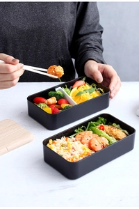 Detail of a black double-layer lunch box featuring divided compartments with fresh food