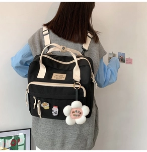Rear view of model wearing a black canvas backpack with cream straps and cute plush pendant