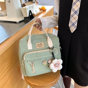 Detail of light green canvas crossbody bag with multiple zip pockets and floral plush pendant