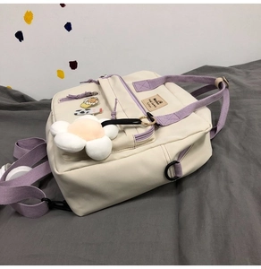 Detail of off-white canvas bag with purple straps, floral charm and cute cartoon badges