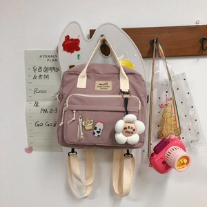 Detail of purple canvas crossbody bag with decorative pins, flower charm, and multi-pockets