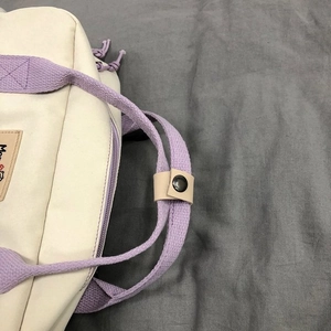 Close-up of beige canvas bag featuring light purple woven handles with a leather snap strap