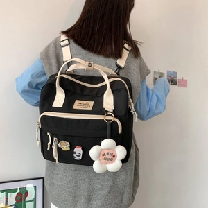 Detail view of the black and beige canvas backpack featuring a floral plush pendant