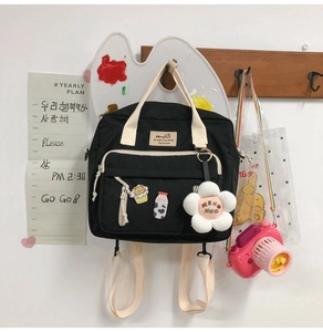 Detail of black canvas tote with cream straps, flower charm and cute cartoon badges