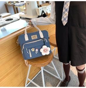 Blue canvas tote bag with cream handles and cute floral charm in a cafe setting