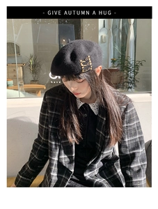Detail shot of black wool beret featuring three parallel gold metal safety pin accents