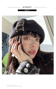 Detail of black wool beret featuring retro gold safety pin accents and elegant texture