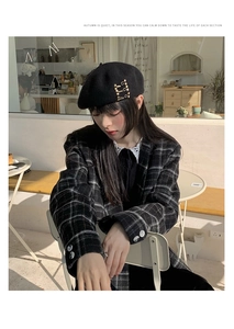 Detail of a black wool beret featuring elegant gold pin accents and metal buckles