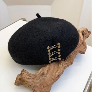 Classic black wool beret with retro metal buckle detail on a minimalist wood stand