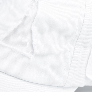 Macro shot of distressed white cotton twill fabric with vintage ripped details on baseball cap