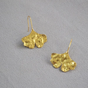 Detailed view of golden ginkgo leaf earrings with textured matte finish on fabric