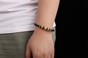 Close-up of a black braided leather bracelet with engraved gold beads on a male model