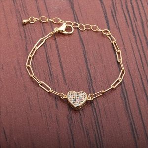 Bracciale a graffetta dorato con ciondolo a cuore pavé arcobaleno su sfondo di legno