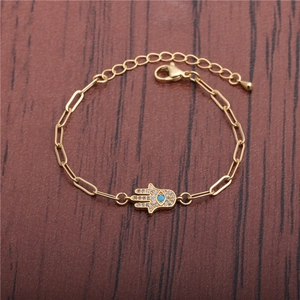 Golden Hamsa Hand bracelet with colorful zircons and blue stone on dark wood background