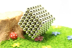 Macro shot of silver magnetic balls formed into a hexagonal prism on a green lawn