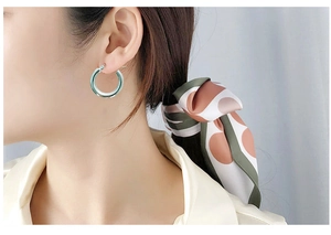 Close-up of a model wearing minimalist thick round green hoop earrings with glossy finish
