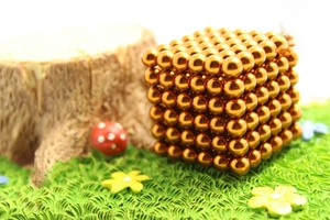 Macro shot of 216 golden 5mm magnetic beads in a 6x6x6 cube on a decorative lawn
