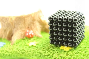 Macro detail of 5mm black magnetic buckyballs arranged in a cube on a rustic surface